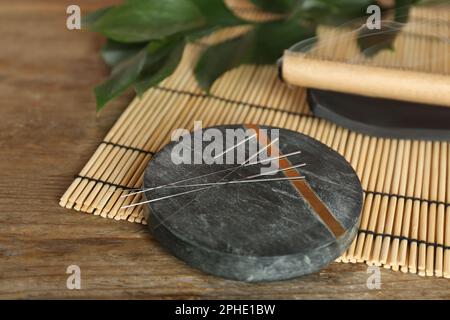 Dessous de verre en pierre grise avec aiguilles d'acupuncture sur une table en bois Banque D'Images