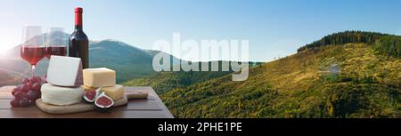 Vin savoureux, raisins et fromages sur table en bois contre beau paysage de montagne, espace pour le texte. Bannière Banque D'Images