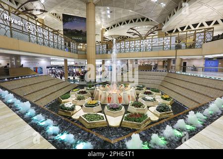 Aéroport international King Khalid, Riyad, Arabie Saoudite : hall d'entrée de la zone de départ, fontaine d'eau intérieure et fleurs, architecture moderne et dorée Banque D'Images