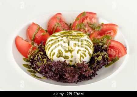 Fromage burrata avec tomates et légumes frais sur une assiette en porcelaine blanche Banque D'Images