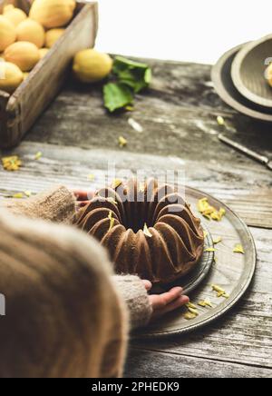 Grand angle de la personne méconnaissable dans des vêtements chauds plaçant le gâteau dans l'assiette sur une table en bois avec des citrons dans la boîte dans la cuisine à la maison Banque D'Images