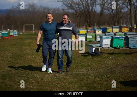 Deux hommes, un beekeper et son ami photographe, regardant les ruches d'abeilles dans un jour ensoleillé de printemps Banque D'Images