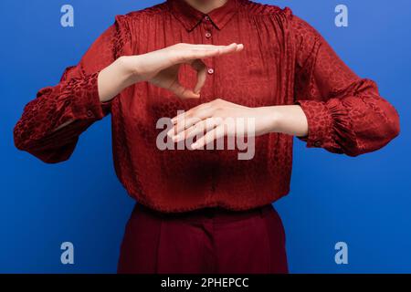 vue rognée de la femme dans un chemisier rouge parlant sur le langage des signes isolé sur bleu, image de stock Banque D'Images