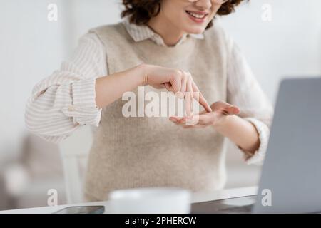 vue rognée de la femme souriante montrant le mot du stand tout en enseignant la langue des signes pendant la leçon en ligne sur ordinateur portable, image de stock Banque D'Images