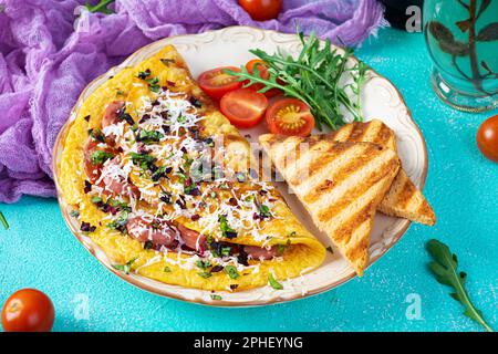 Omelette frite farcie à la saucisse, aux tomates, aux légumes verts et au fromage. Délicieux petit déjeuner facile Banque D'Images