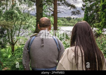 Photo de l'arrière d'un couple de parents marchant dans la nature au jardin du Dr Neil à Édimbourg au printemps. Le père porte un porte-bébé. MUL Banque D'Images