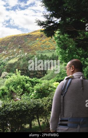 Photo verticale de l'arrière d'un nouveau parent mâle avec un porte-bébé marchant dans la nature avec des lunettes. Famille multiculturelle et multiethnique britannique. Banque D'Images