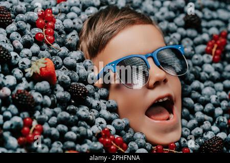 Visage de petit garçon souriant dans des baies mûres bleuets, plante de myrtille biologique Banque D'Images