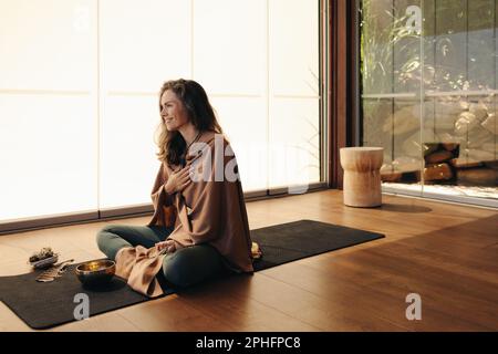 Bonne femme âgée méditant en utilisant la médecine alternative à la maison. Femme mature pratiquant une cérémonie d'auto-guérison et de purification sur un tapis de yoga. Cheerfu Banque D'Images