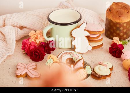 Table de Pâques confortable et esthétique avec tasse à lait avec biscuits glacés, gâteau et fleurs. Printemps vacances fond floral Banque D'Images