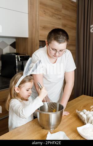 Frère enseignant la cuisine de soeur, enfant mélangeant la pâte dans les oreilles de lapin dans la cuisine. Pâques, fête des mères et des pères, concept de soutien familial Banque D'Images