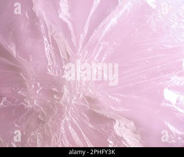 Image en gros plan d'un film de cellophane en plastique fondu transparent sur fond rose. Motif abstrait de polyéthylène texturé fusionné. Format horizontal. Banque D'Images