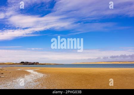 Vue sur le sable jusqu'au fort Belan avec la plage de Newborough sur Anglesey en traversant le détroit de Menai. Dinas Dinlle, Caernarfon, Gwynedd, nord du pays de Galles, Royaume-Uni, Grande-Bretagne Banque D'Images