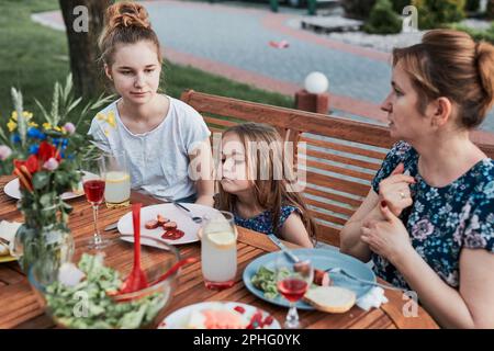 Famille ayant un repas du grill pendant le pique-nique d'été dîner en plein air dans un jardin de maison. Gros plan des personnes assises à une table avec de la nourriture et de la vaisselle Banque D'Images