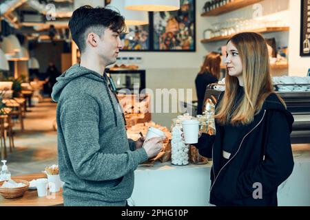 Amis qui ont un chat, tenant des tasses de café, debout dans un café et attendant les commandes. Homme et femme ayant une pause boire un café au café Banque D'Images