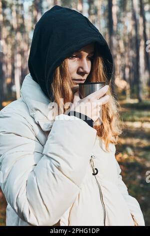 Femme dans une hotte ayant une pause pendant le voyage d'automne tenant une tasse avec une boisson chaude de thermos fiole le jour d'automne froid. Fille active errant dans une forêt ac Banque D'Images