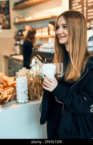 Femme tenant une tasse de café, debout dans un café et attendant la commande. Jeune femme souriante ayant une pause boire un café au café Banque D'Images