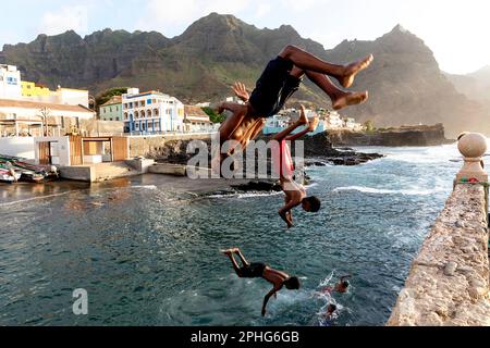 Des garçons du coin sautant de la jetée à la mer dans le port de Ponta do sol avec des montagnes spectaculaires à l'arrière-plan, Santo Antao, Cabo verde Banque D'Images