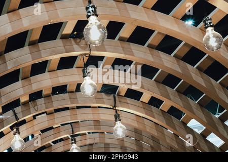 De nombreuses ampoules blanches sont accrochées au plafond de la structure en bois de Pergola courbée. Ampoules en façade en bois Architecture. Espace pour le texte, Sél Banque D'Images