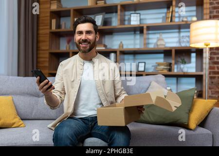 Portrait d'un acheteur en ligne heureux à la maison, homme adulte mûr souriant et regardant l'appareil photo, tenant la boîte de produit et le téléphone, heureux de la livraison rapide de la boutique en ligne. Banque D'Images
