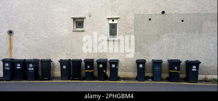 Longue rangée (13) de poubelles domestiques noires pour la collecte le long de la rue par mur de maison, Bristol, Royaume-Uni Banque D'Images