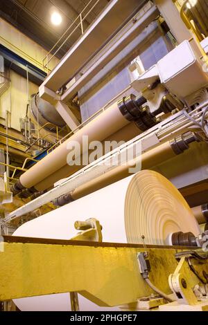 De gros rouleaux de papier sortent de la machine dans une usine de papeterie. Banque D'Images