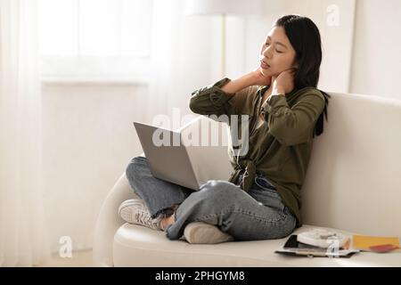 Femme asiatique surtravaillée indépendante assise sur un canapé avec un ordinateur portable Banque D'Images