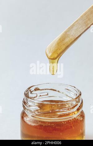 Pâte de sucre pour l'épilation à couper dans un pot en verre avec une spatule en bois sur fond blanc. Miel naturel Banque D'Images