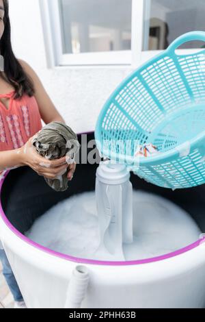 Une jeune femme hispanique essait le savon d'une chemise verte sur un lave-linge à chargement par le haut Banque D'Images