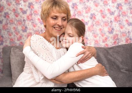 Une grand-mère âgée affectueuse embrasse et embrasse sa petite-fille adolescente, assise sur le canapé. Banque D'Images