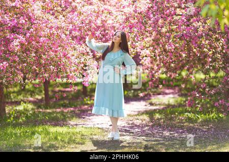 Appréciant la fille de brunette en robe bleue, dans un jardin rose en fleur Banque D'Images