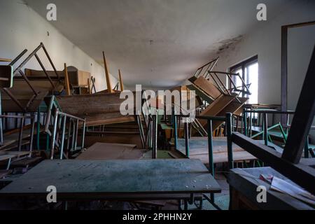 Des bureaux d'école dispersés et rentournés dans une salle de classe abandonnée Banque D'Images