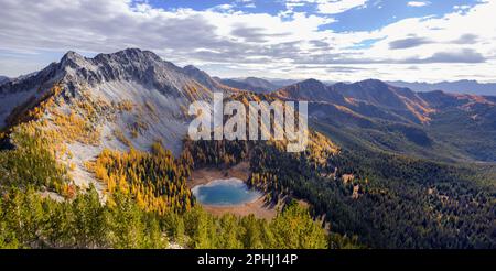 Le coucher du soleil illumine les larches d'or, les sommets de montagne et un lac alpin dans la région sauvage de Chelan Sawtooth. Cascades du Nord, Washington Banque D'Images