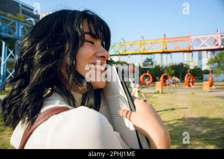 jeune femme latine, vénézuélienne, étudiante à l'université, heureuse de ses études, elle embrasse son livre, debout à l'extérieur, au coucher du soleil. Banque D'Images