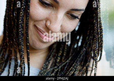 Portrait rapproché d'une fille tenant le rire, regardant vers le bas. Concentrez-vous sur son petit anneau de perçage de nez, des taches de rousseur, et des cheveux de boîte-tresse. Bien entretenu Banque D'Images