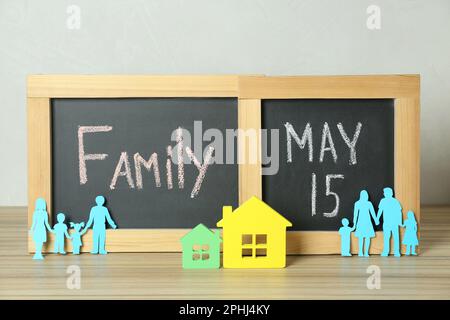 Bonne journée en famille. Tableaux noirs, parents en papier et leurs enfants près des modèles de maison sur une table en bois Banque D'Images