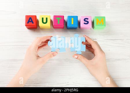 Femme tenant des pièces de puzzle près des cubes avec le mot Autism à la table blanche en bois, vue de dessus Banque D'Images