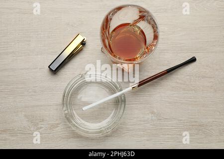 Cendrier en verre avec porte-cigarettes long, briquet et boisson alcoolisée sur table en bois, plat Banque D'Images