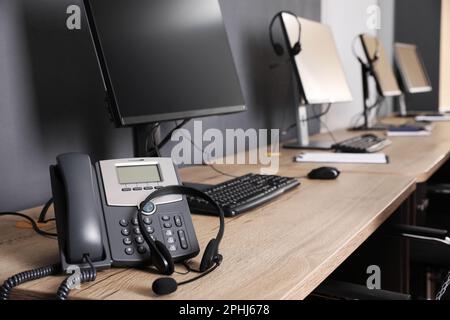 Téléphone fixe et casque près d'un ordinateur moderne sur un bureau en bois. Service d'assistance téléphonique Banque D'Images