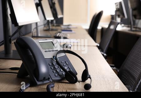 Téléphone fixe et casque près d'un ordinateur moderne sur un bureau en bois. Service d'assistance téléphonique Banque D'Images