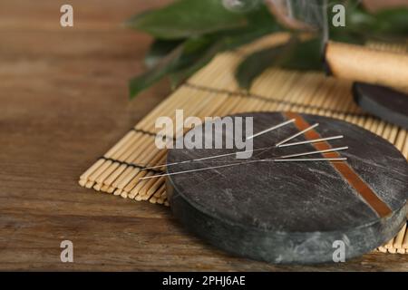 Dessous de verre en pierre grise avec aiguilles d'acupuncture sur une table en bois. Espace pour le texte Banque D'Images