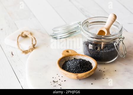 Sel de roche hawaïen noir dans un petit bol et un pot, sur un plateau en marbre blanc. Banque D'Images