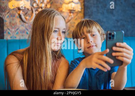 Une jeune maman attentionnée s'assoit sur un canapé dans la salle de séjour avec un petit fils regarde une drôle de dessin animé sur un smartphone, une mère heureuse ou une nounou se détend sur un canapé avec peu de choses à la maison Banque D'Images