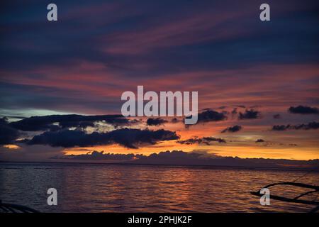 Coucher de soleil pittoresque sur la plage de l'île Pamilacan aux Philippines, le ciel nuageux brille dans les couleurs orange pêche dorée, rouge et bleu. Banque D'Images