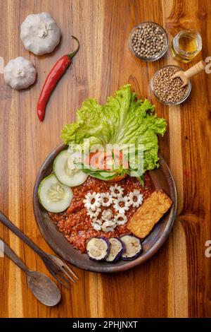 Calamars frits croustillants avec sauce Chili épicée ou sambal dans une assiette en poterie sur une table en bois Banque D'Images