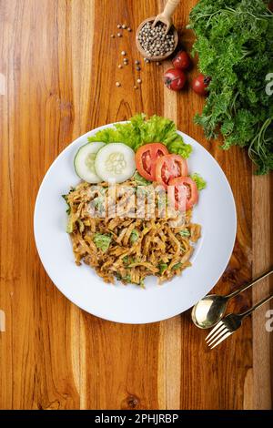 Remuez les nouilles ou le mie goreng avec les légumes, le poulet, l'œuf et le bœuf dans une assiette blanche à table en bois Banque D'Images
