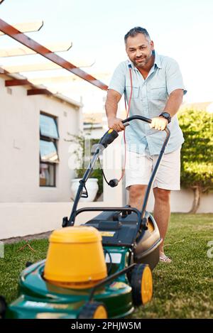 Temps de coupe de l'herbe. Portrait d'un homme joyeux d'âge moyen qui coupe de l'herbe avec une tondeuse tout en regardant la caméra à la maison. Banque D'Images
