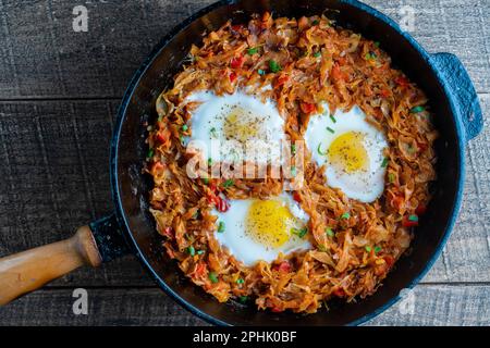Ragoût de chou avec des légumes et des œufs frits dans une poêle sur fond de bois, gros plan, vue de dessus. La nourriture. Une alimentation saine Banque D'Images