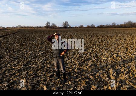 Agriculteur senior debout dans un champ labouré par beau temps d'hiver Banque D'Images