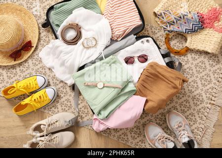 Ouvrez la valise pleine de vêtements et d'accessoires d'été près des chaussures au sol, vue du dessus Banque D'Images